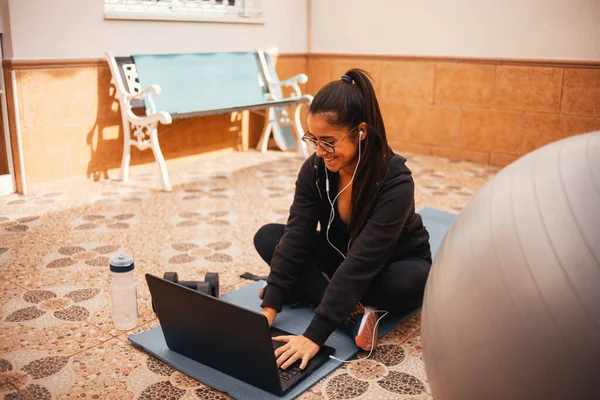 Evde dizüstü bilgisayarla egzersiz yapan bir kadın. Sağlıklı kadın yoga tahtası yapıyor ve dizüstü bilgisayardan online dersler izliyor.