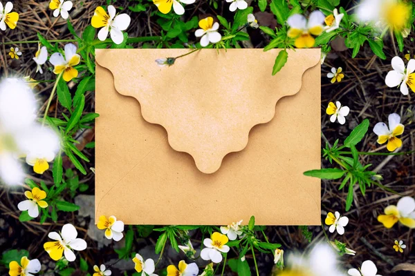 Wykonać makietę koperty z żółtym kwiatem i zielonymi liśćmi na ziemi przyrody. Leżeć płasko. Widok z góry na liść — Zdjęcie stockowe
