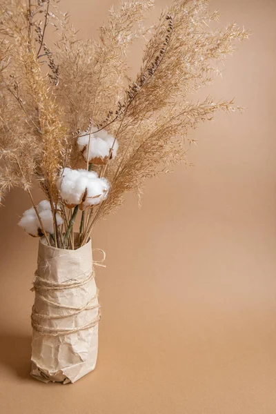 Bouquet of pampas grass and cotton flowers on beige background in craft vase. Boho style bouquet. Eco flower composition . High quality photo