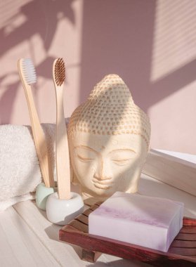 Beyaz Buda, gölgelerle süslenmiş pastel pembe arka planda büstü. Bambu diş fırçasına sıfır atık. Asya usulü spa. Sakin ol. Yoga arka planı. Çevre dostu. Yüksek kalite fotoğraf
