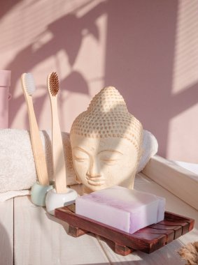 Beyaz Buda, gölgelerle süslenmiş pastel pembe arka planda büstü. Bambu diş fırçasına sıfır atık. Asya usulü spa. Sakin ol. Yoga arka planı. Çevre dostu. Yüksek kalite fotoğraf