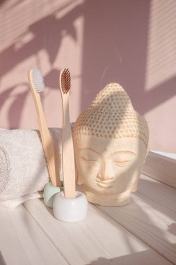 Beyaz Buda, gölgelerle süslenmiş pastel pembe arka planda büstü. Bambu diş fırçasına sıfır atık. Asya usulü spa. Sakin ol. Yoga arka planı. Çevre dostu. Yüksek kalite fotoğraf