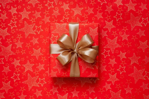 Luxury Christmas gift box wrapped in red paper decorated with golden star pattern. New year web banner or wallpaper. Present decorated with golden bow and ribbon. Simple and modern Marry Christmas box