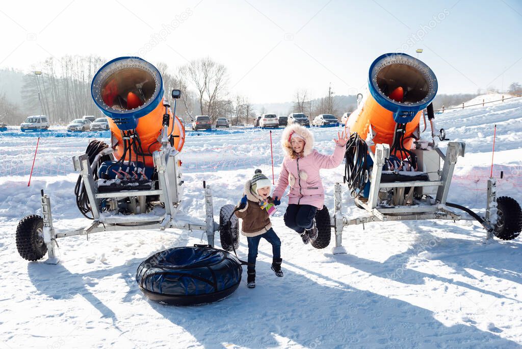 boy and girl jumping near the snow cannon and tubing