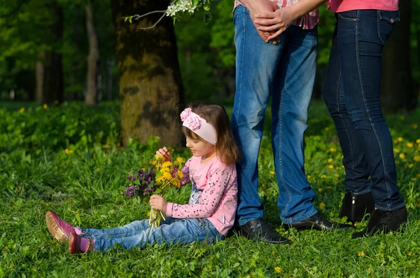 Ένα κορίτσι συλλέγει τα λουλούδια τομέα σε μια ανθοδέσμη κάθεται κοντά οι γονείς — Φωτογραφία Αρχείου