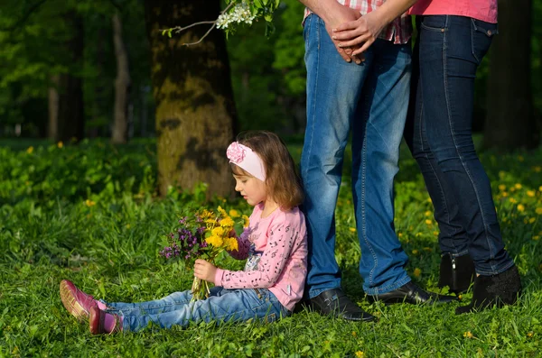 Una chica recoge las flores del campo en un ramo se sienta cerca de los padres — Foto de Stock