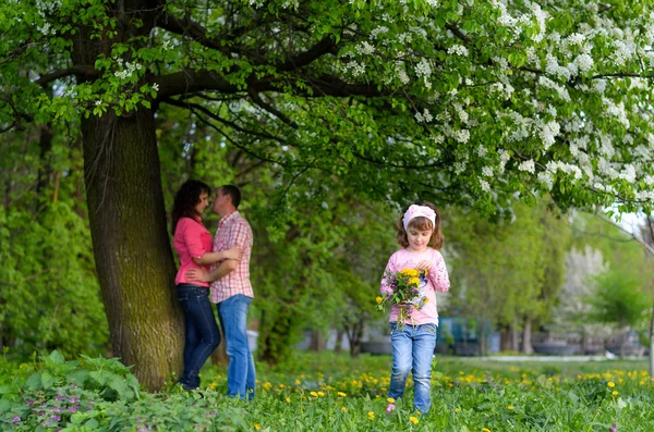 Ein Mädchen sammelt die Feldblumen in einem Strauß sitzt neben den Eltern — Stockfoto
