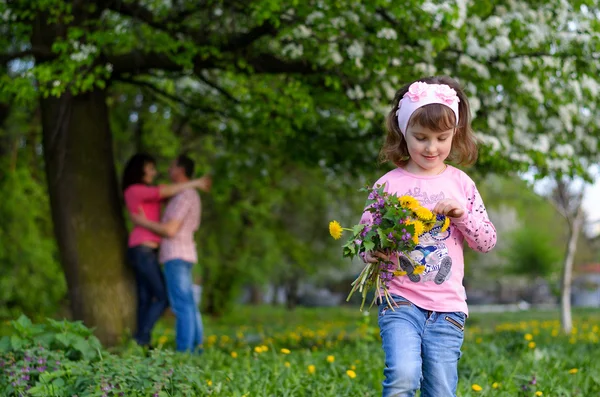 Uma menina coleta as flores do campo em um buquê fica perto dos pais — Fotografia de Stock
