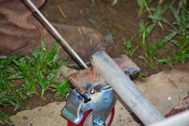 Kaynak makinesi olan bir işçi etrafta uçuşan kıvılcımları olan tekerlekleri tamir ediyor.