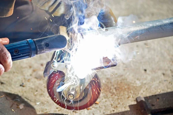 Worker with a welding machine fixing a caster wheels with fiery sparks flying around