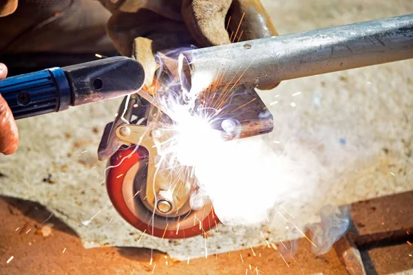 Worker with a welding machine fixing a caster wheels with fiery sparks flying around