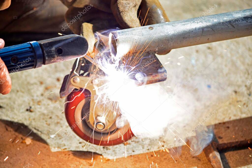Worker with a welding machine fixing a caster wheels with fiery sparks flying around