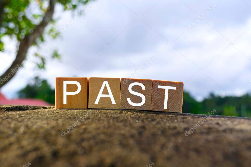 Past text on wooden cube block on top of big stone with blurred sky background