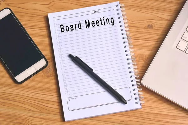 Board meeting label on notepad with laptop and smartphone on wooden table. Business concept