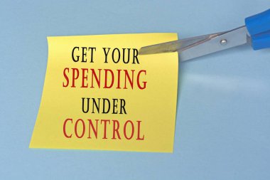 Sarı not defterini mavi arkaplandaki yazıyla kesen makas. Harcama kavramı