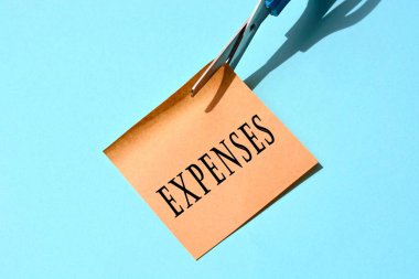 Masraflarla dolu sarı not defterini mavi arka planda kesen makas. Harcama kavramı