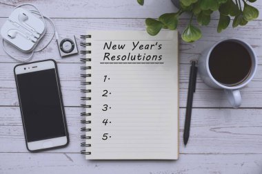 Not defterine bir fincan kahve, akıllı telefon, müzik çalar ve tahta masadaki kalemle birlikte mesaj at. Yeni Yıl Kararları Konsepti