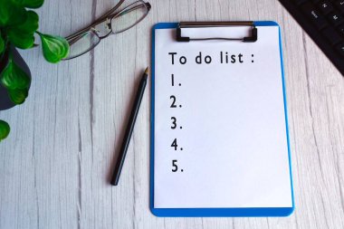 To do list text on blue clip board with glasses, pen, plant and keyboard on wooden desk.  clipart