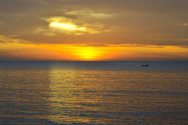 Sahilde akşam güneşi batıyor ve balıkçı uzaktan balık tutuyor.