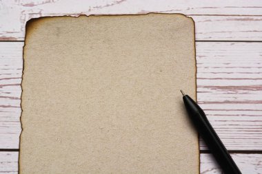 Ahşap masasında kalem olan yanık kenarlı kahverengi kağıt.