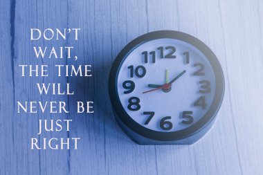 Ahşap masada siyah alarmlı saat ile motive edici bir alıntı.