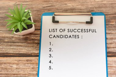Text on blue clip board with potted plant on wooden desk - List of successful candidates clipart