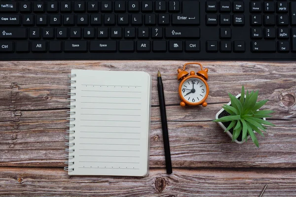 Notepad with pen, alarm clock, potted plan and keyboard on wooden desk — Stock Photo, Image