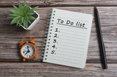 Not defterinde kalem, alarm saati ve tahta masanın üzerine saksı bitkisi olan metin