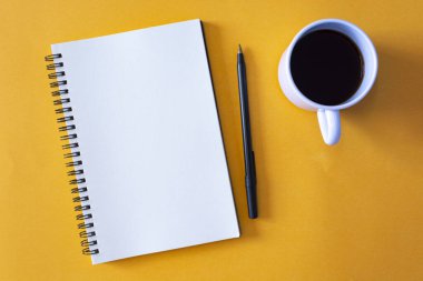 Kalemli not defteri ve sarı arka planda bir fincan kahve. Metin kullanımı için
