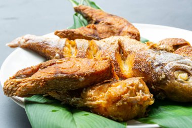 Koyu arka planda yeşil yapraklı kızarmış balık.