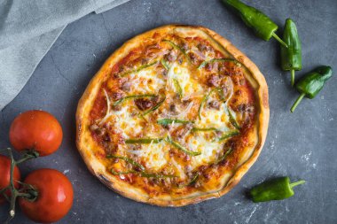 Domatesli, biberli, soğanlı ve malzemelerle çevrili ev yapımı pizzanın genel görünümü