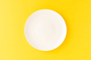 Sarı masadaki boş beyaz tabağın yukarıdan görüntüsü. Kapat.