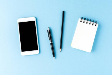 Akıllı telefon, defter ve kalemler mavi masaüstüne. İş geçmişi