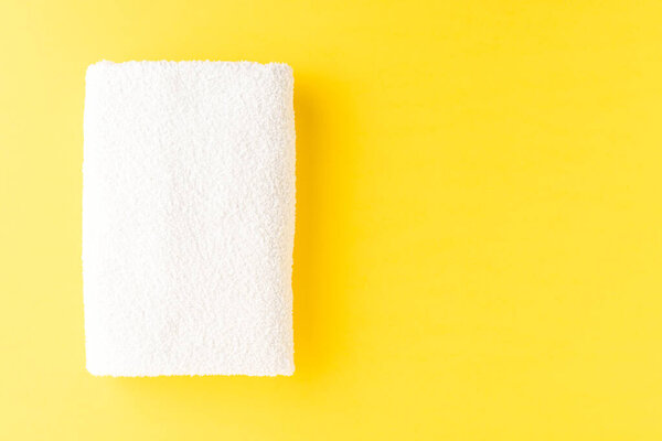 White spa towel on yellow background with copyspace. Top view