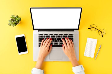 Kadın eli boş bir ekranla dizüstü bilgisayarda çalışıyor. Cep telefonu, defter, kalem ve gözlüklü iş geçmişi. Üst görünüm