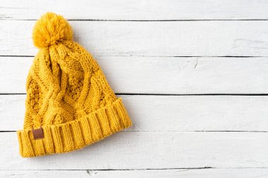 Beyaz ahşap arka planda, kopyalanmış püsküllü sarı kış şapkası. Üst görünüm