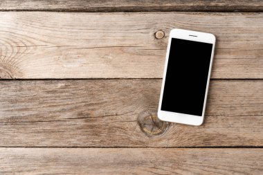 Ahşap masadaki boş ekranlı akıllı telefon. Üst görünüm
