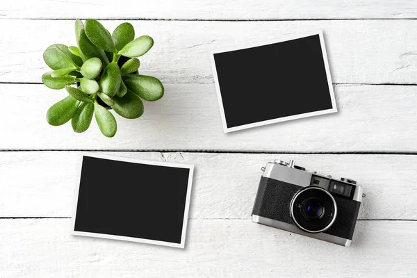 Empty photo frames with vintage camera on white wooden background. Top view