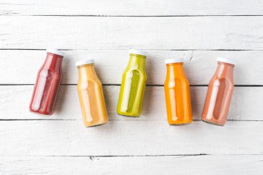 Telif alanı olan beyaz ahşap masada renkli meyve suları. Şişelerdeki taze sıvılar