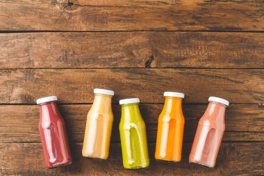 Kopyalama alanı olan eski ahşap masada renkli meyve suları. Şişelerdeki taze sıvılar
