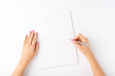 Beyaz arka planda izole edilmiş boş kağıtların üzerine kalemle yazı yazan kadın elleri. Üst görünüm