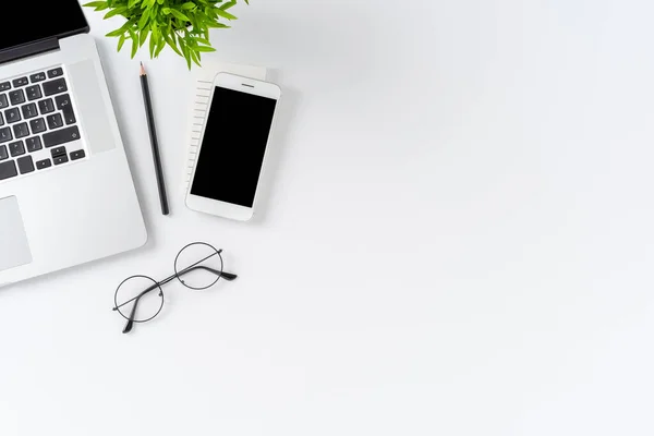 Office desktop with laptop, mobile phone and eyeglasses on white background with copyspace. Flat lay