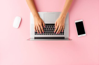Akıllı telefon ve bilgisayar faresiyle pembe masada dizüstü bilgisayar kullanan kadın elleri. İş geçmişi. Üst görünüm