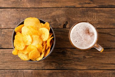 Tahta masadaki kasede bir bardak bira ve patates cipsi. Üst görünüm