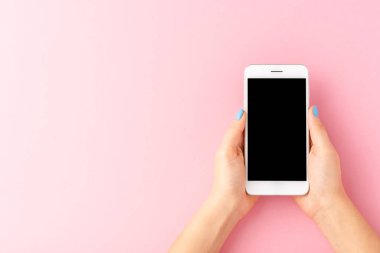Kadın elleri pembe arka planda boş ekranlı cep telefonu kullanıyor. Üst görünüm