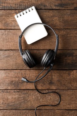 Ahşap masaüstünde defter olan yardım masası kulaklıkları. Çağrı merkezi konsepti. Üst görünüm