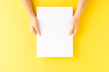 Sarı zemin üzerinde boş kağıt çarşaf tutan kadın elleri.