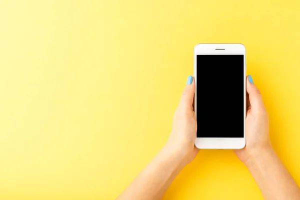 Kobiece Ręce Trzymające Smartfon Pustym Ekranem Żółtym Tle Widok Góry — Zdjęcie stockowe