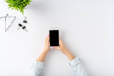 Beyaz masanın üzerinde boş ekranı olan akıllı telefon kullanan kadın elleri. Ofis masaüstü. Düz yatıyordu
