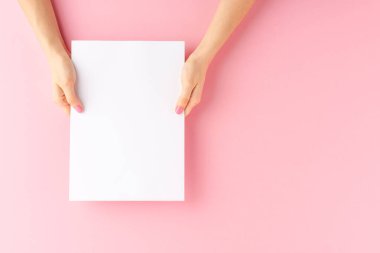 Kadın elleri pembe arka planda kopyalama alanı olan beyaz kağıt gösteriyor. Kapat.